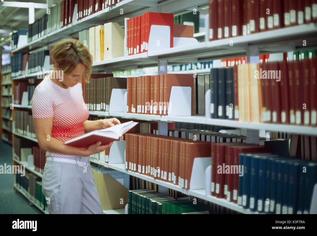 Frau liest Buch im Bücherregal in einer Bibliothek Stockfoto