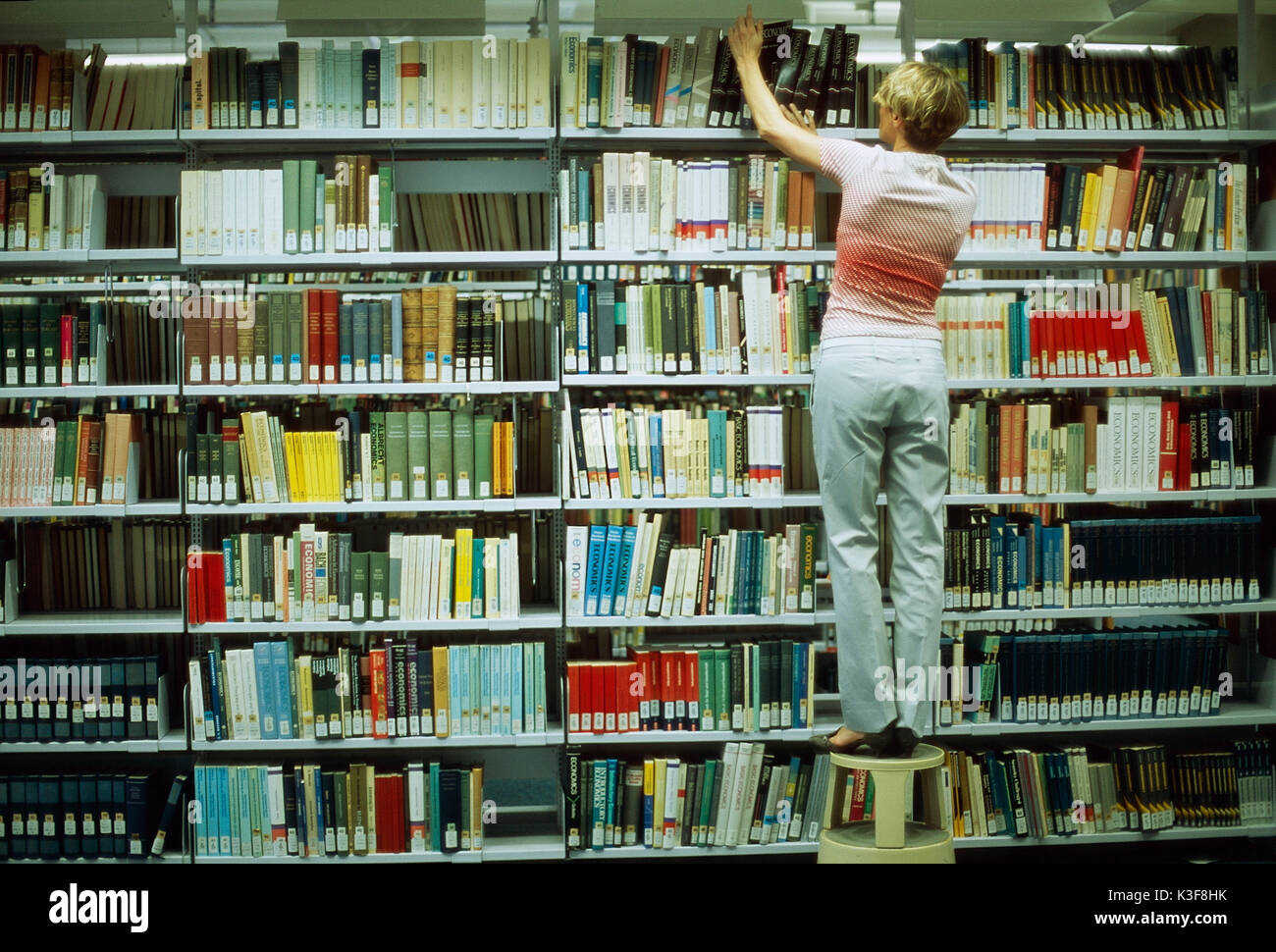 Frau sucht Buch im Bücherregal einer Bibliothek Stockfoto