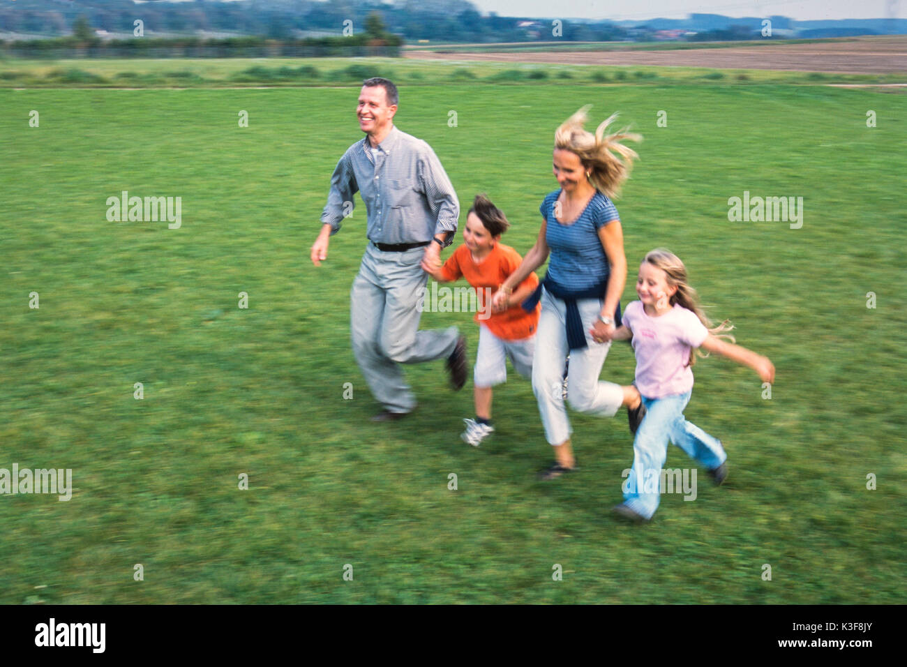 Junge Familie läuft Hand in Hand über einer Wiese Stockfoto