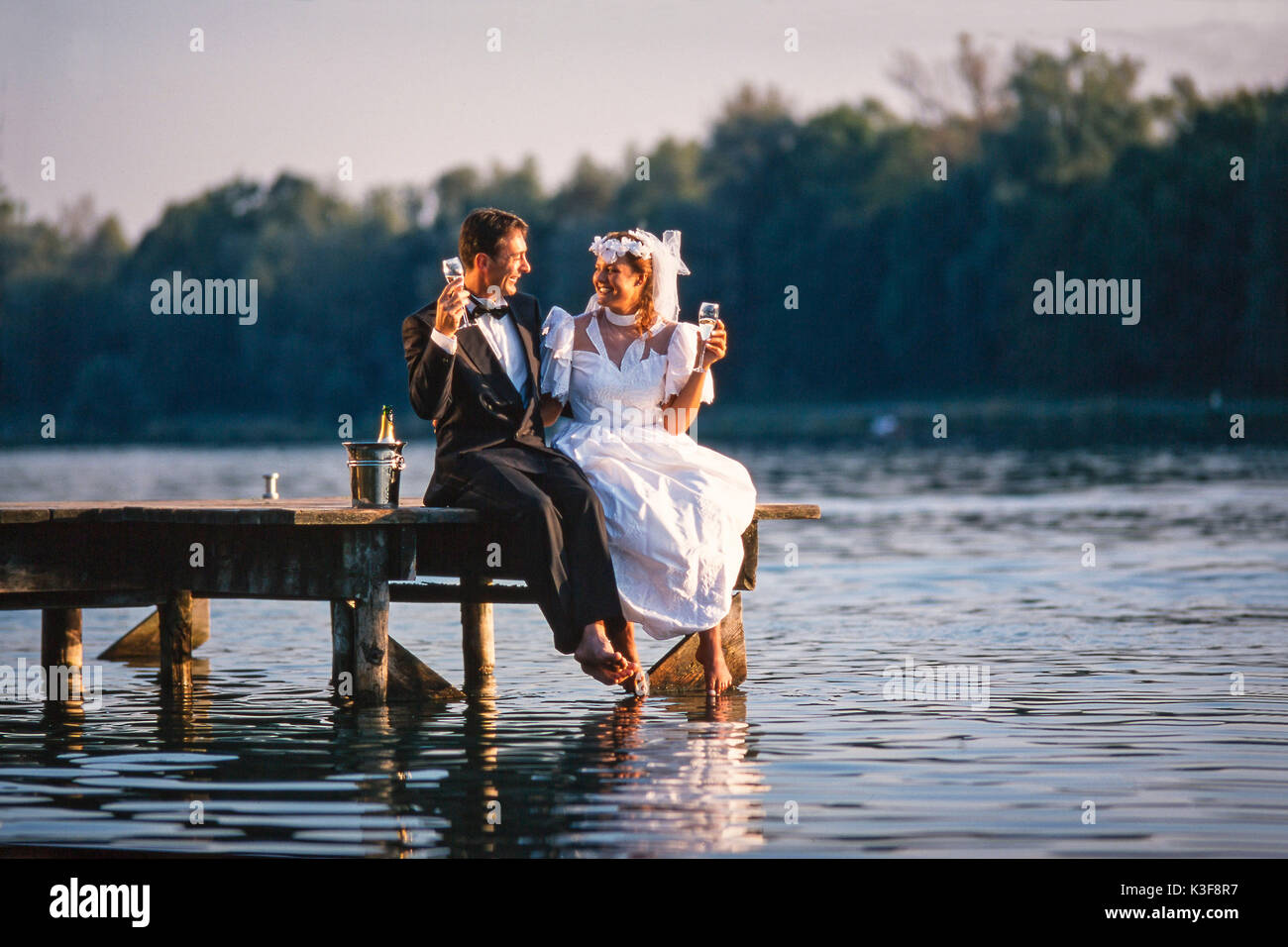 Brautpaar sitzt auf der Brücke mit Champagner Glas in der Hand Stockfoto