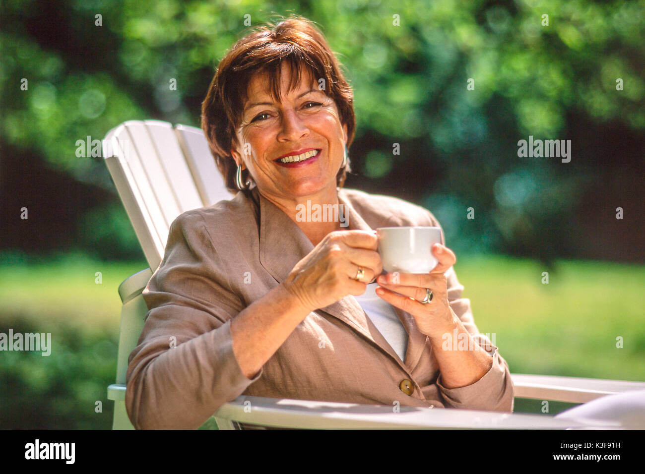 Frau im mittleren Alter sitzt im Garten Stuhl schließen eine Tasse Kaffee in der Hand Stockfoto