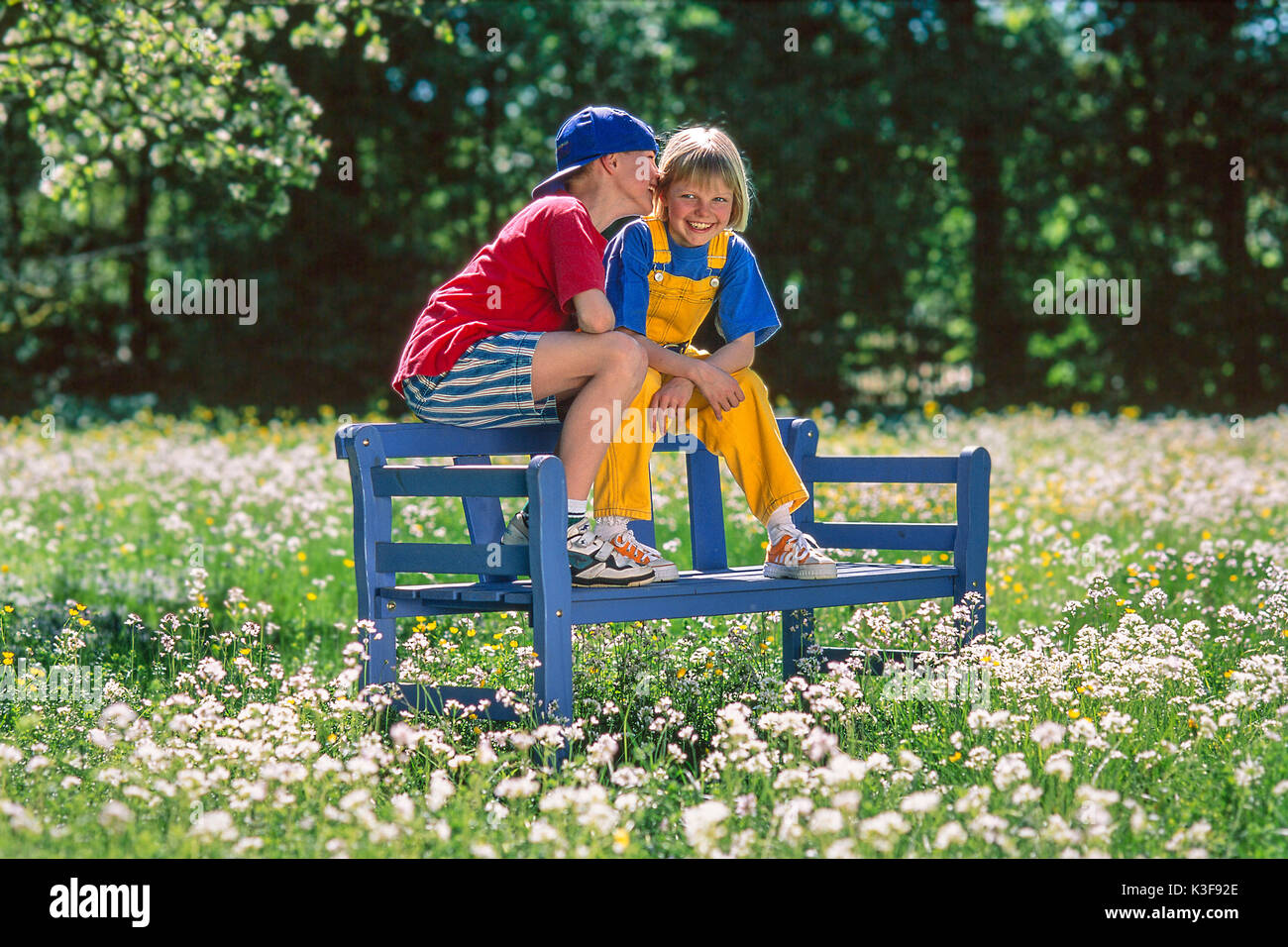 Junge und Mädchen sitzen in einem Garten auf der Armlehne eines Garten Bank und Flüstern Stockfoto