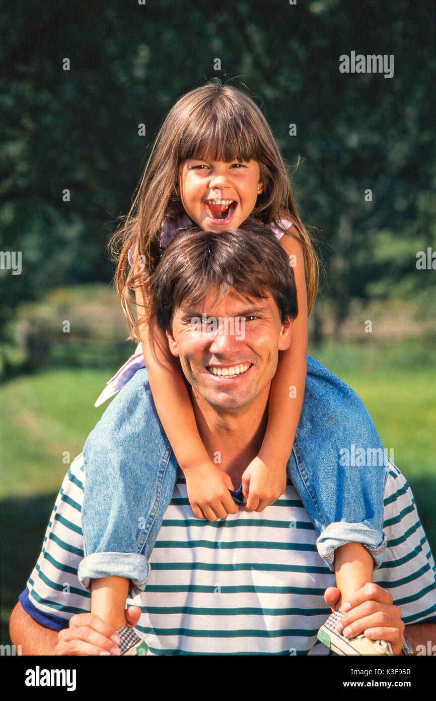 Vater trägt Lachen Tochter mit braunen langen Haaren auf den Schultern Stockfoto