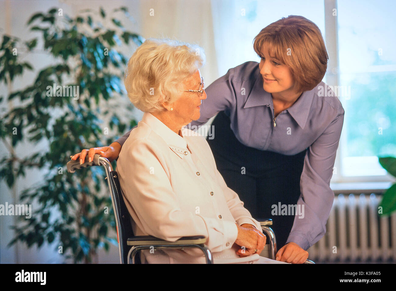 Junge Frau im Gespräch ein Senior in der Nähe, der sitzt im Rollstuhl Stockfoto