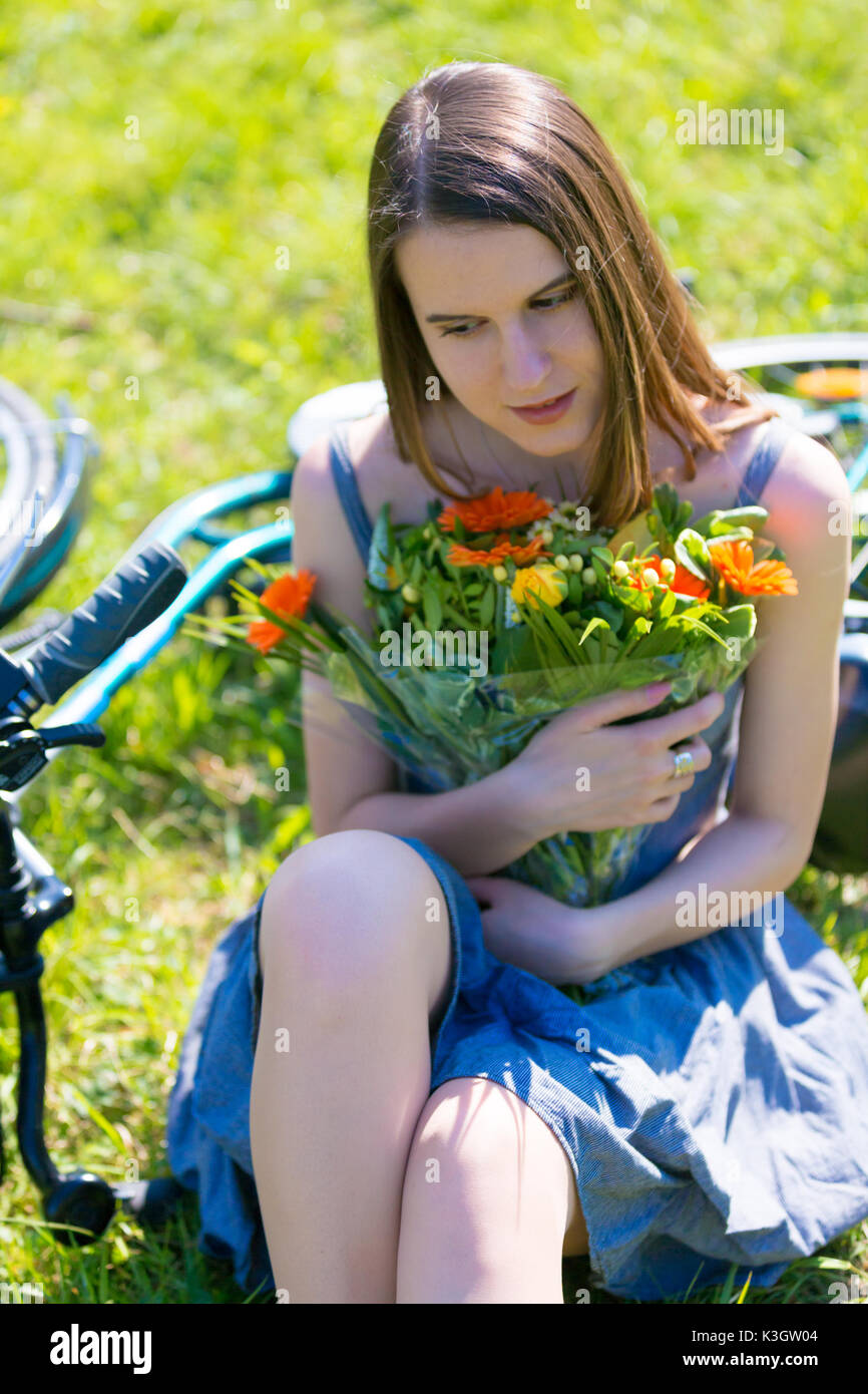 Junge Frau sitzt auf dem Rasen in einem Park in der Nähe ein Fahrrad und ein Blumenstrauß Stockfoto