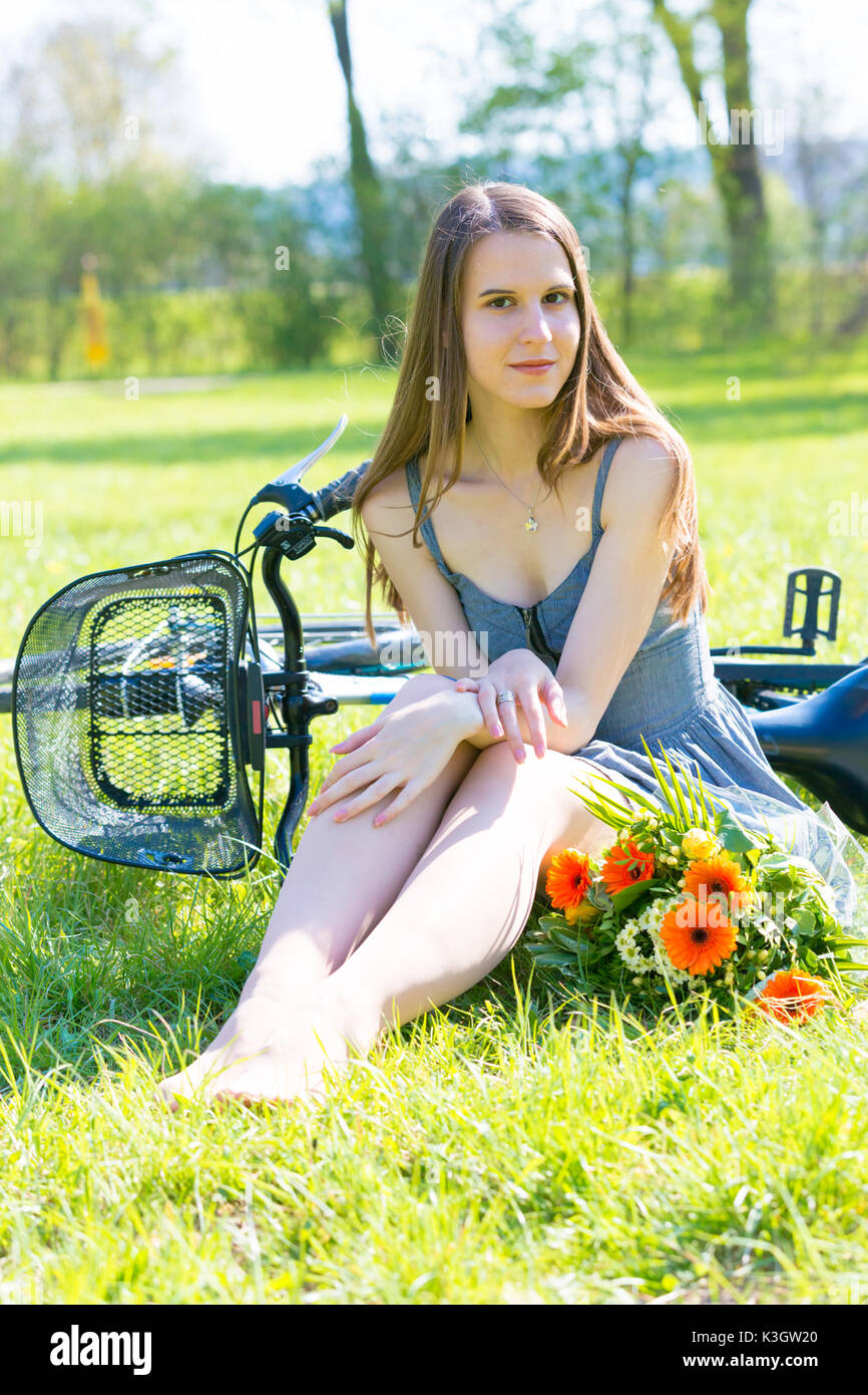 Junge Frau sitzt auf dem Rasen in einem Park in der Nähe ein Fahrrad und ein Blumenstrauß Stockfoto
