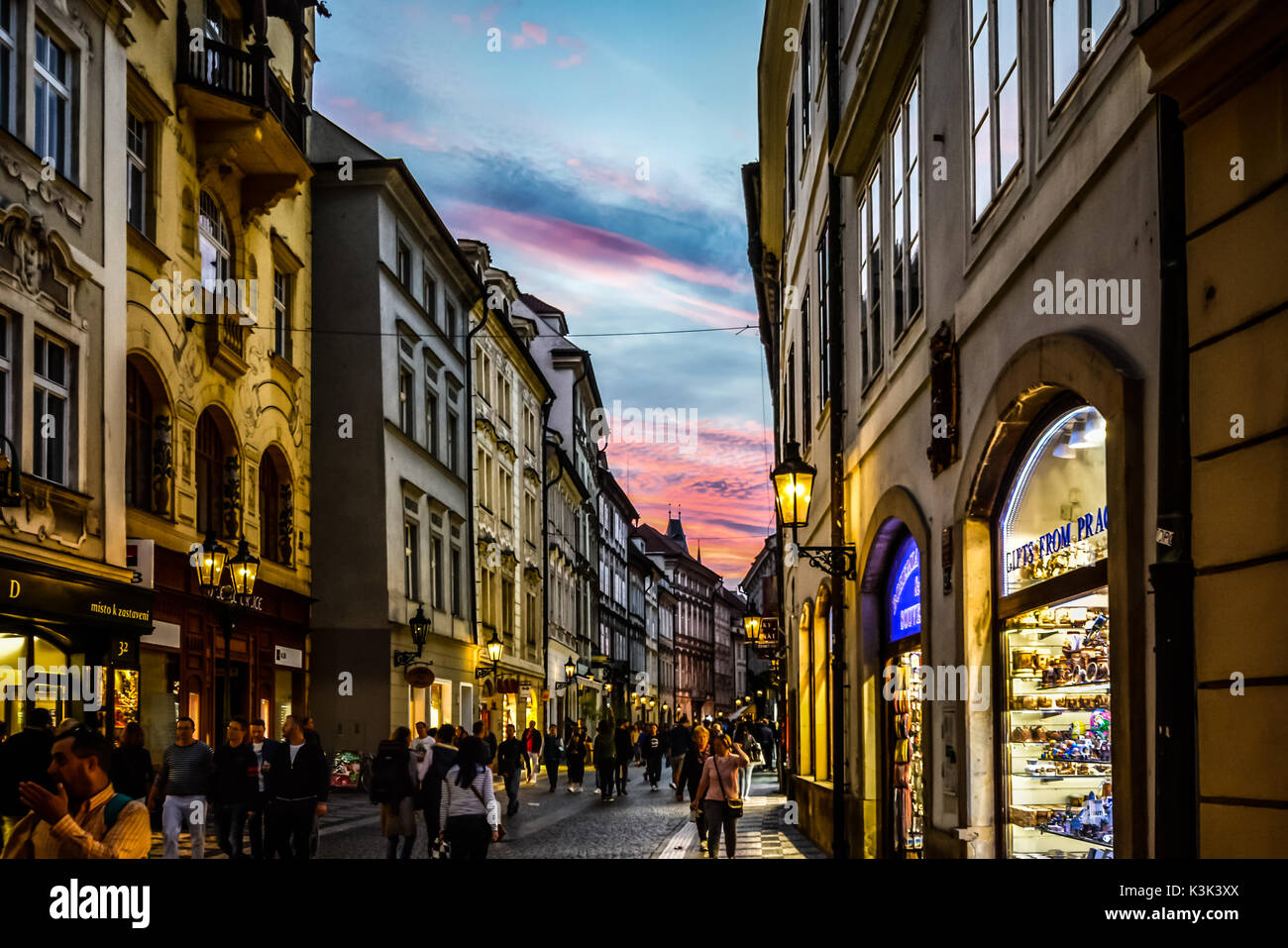 Einer touristischen Straße in der Prager Altstadt, wie die Sonne mit dem Shop Lichter leuchten und eine bunte Himmel in der Ferne Stockfoto