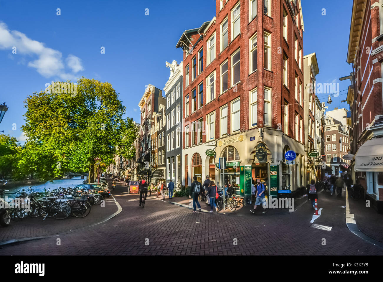 Ein schmales Gebäude, das ein Geschäft auf einer Kreuzung mit einer schmalen Straße liegt an einem Kanal in Amsterdam an einem sonnigen Tag im frühen Herbst Stockfoto