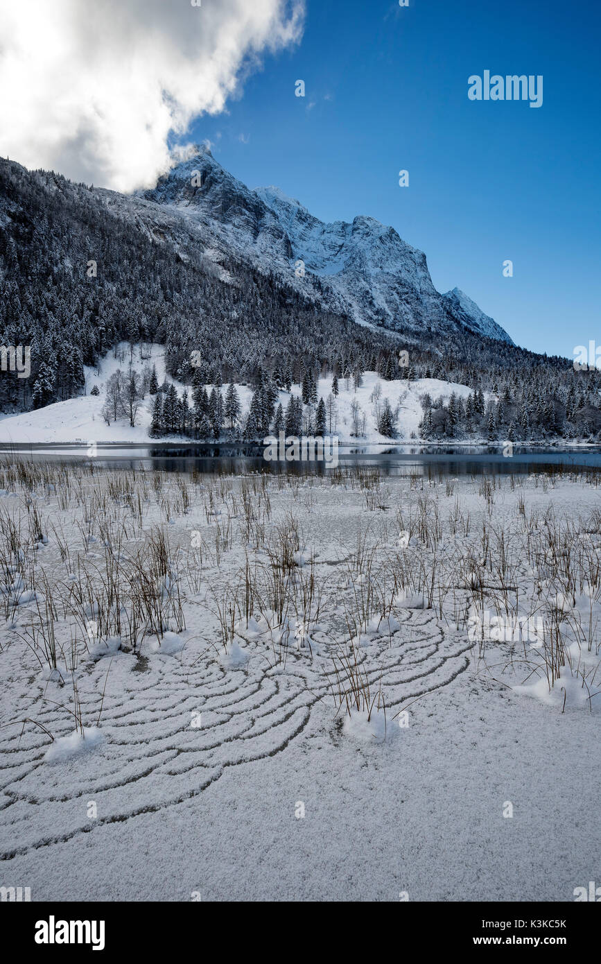 Winter Eindruck am Ferchensee über Mittenwald, mit Schnee und Eis in den Reed. Im Hintergrund Wettersteingebirge. Das Blau des Himmels spiegelt den Schnee auf dem Berg. Stockfoto