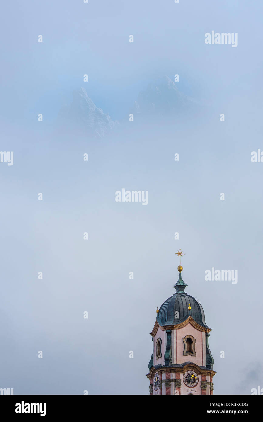 Viererspitze über Mittenwald in der westlichen Karwendel glänzt durch die Wolken, im unteren Teil des Bildes der Turm der Kirche St. Peter und Paul in Mittenwald. Stockfoto