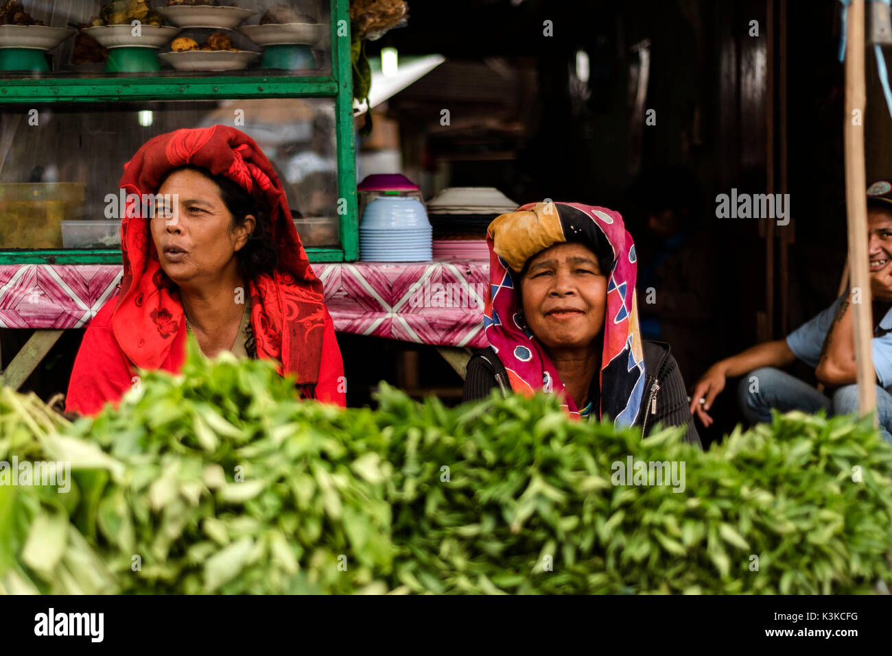 Zwei alte Frauen in ihrer pflanzlichen ausgeht, in der traditionellen Kleidung der Batak ethnische Gruppe. Im Hintergrund gibt es grinst ein Raucher. Auf dem Markt in Berastagi auf Sumatra, Indonesien. Stockfoto