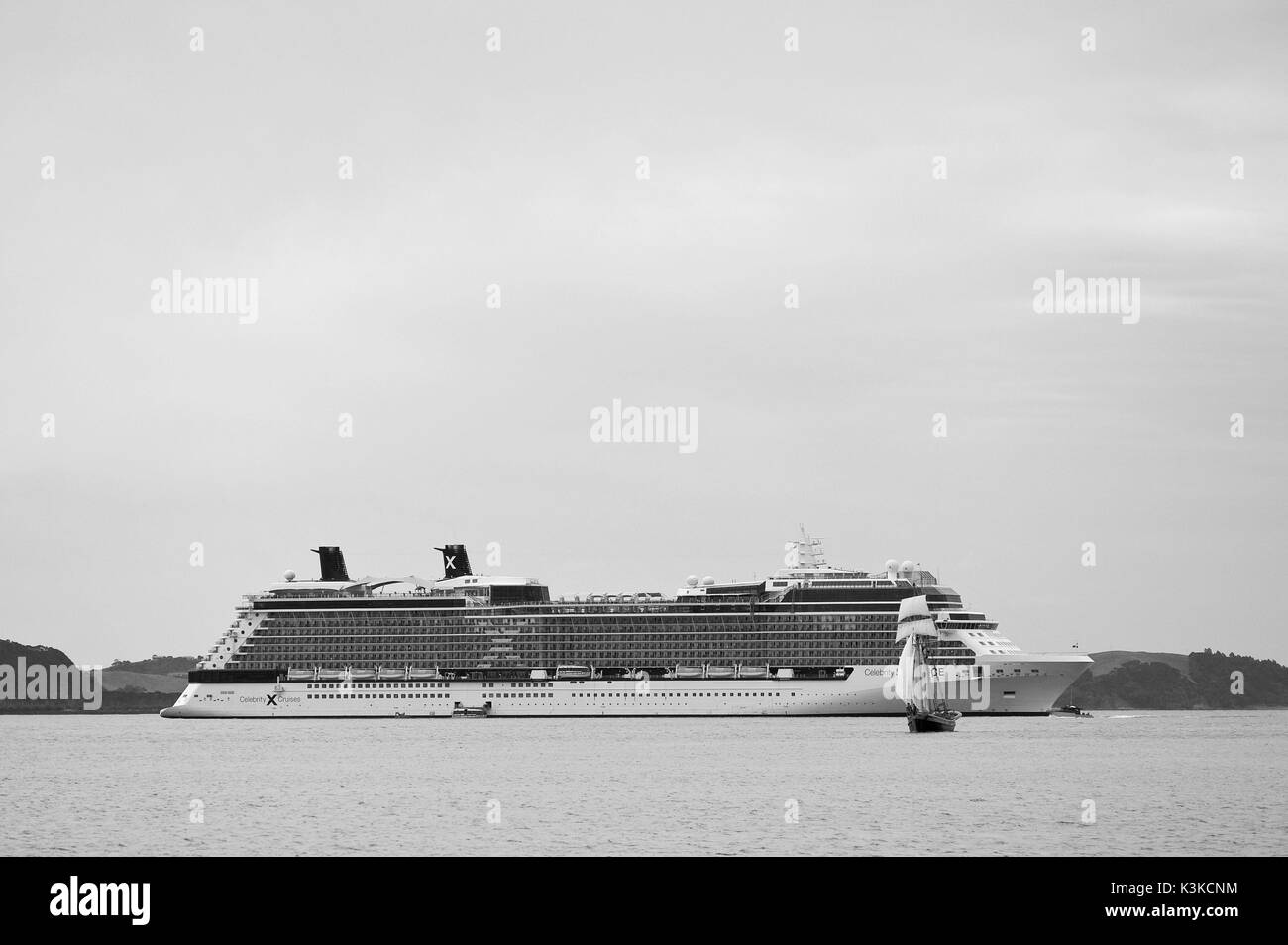 Kleines Segelschiff vor großen Kreuzer in Neuseeland. Stockfoto