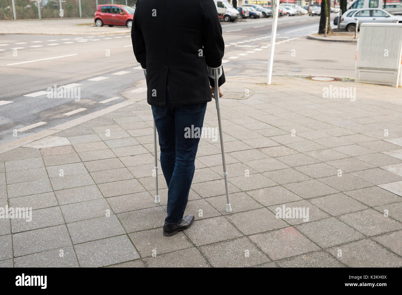 Ansicht von hinten von einem Mann auf der Straße mit Krücken Stockfoto