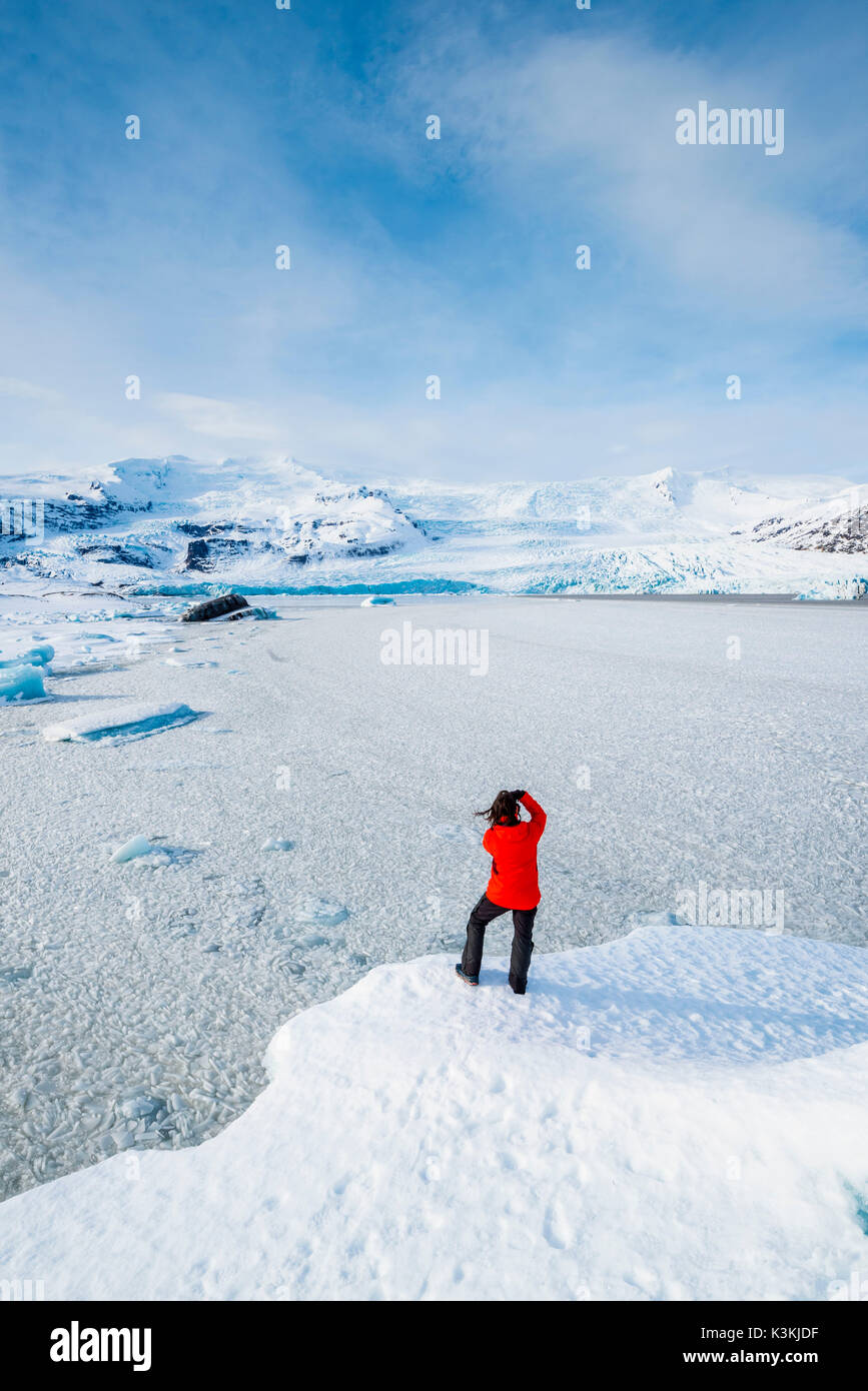 Fjallsarlon Gletscherlagune, Osten Island, Island. Mann mit dem roten Mantel mit Blick auf den gefrorenen Lagune im Winter (HERR). Stockfoto