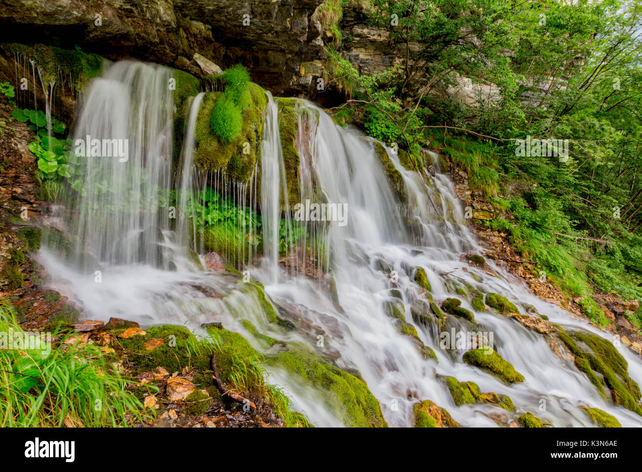 Ephemere Wasserfall im Tal von San Lucano, Agordino, Dolomiten. Das Wasser scheint aus dem Herzen der Berge zu fließen. Rund um das grüne Moos und Pflanzen Merkmal von Feuchtgebieten. Stockfoto