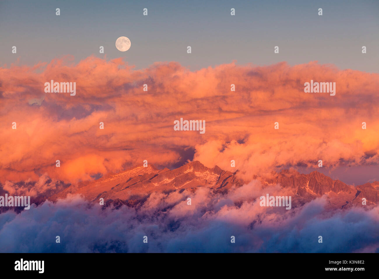 Valli di Sant'Antonio, Lombardei, Italien. Der Vollmond Aufstieg von Adamello Gruppe bei Sonnenuntergang mit Wolken. Stockfoto