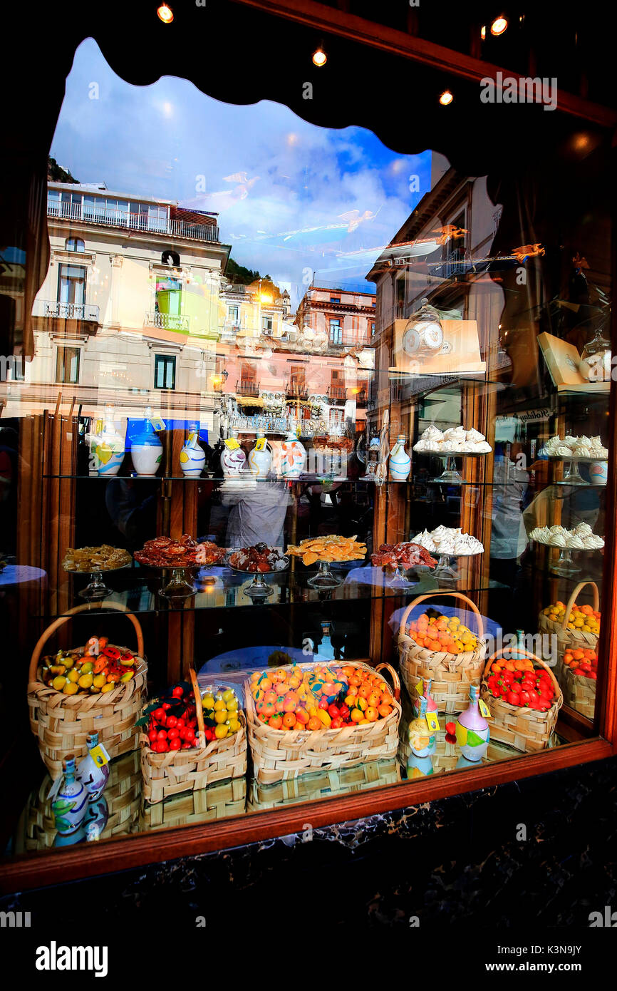 Klassische Fenster eines Süßwaren von Amalfi, mit Blick auf die typischen lokalen Spezialitäten und im Glas die Reflexion der Häuser auf den Platz. Kampanien, Italien Stockfoto