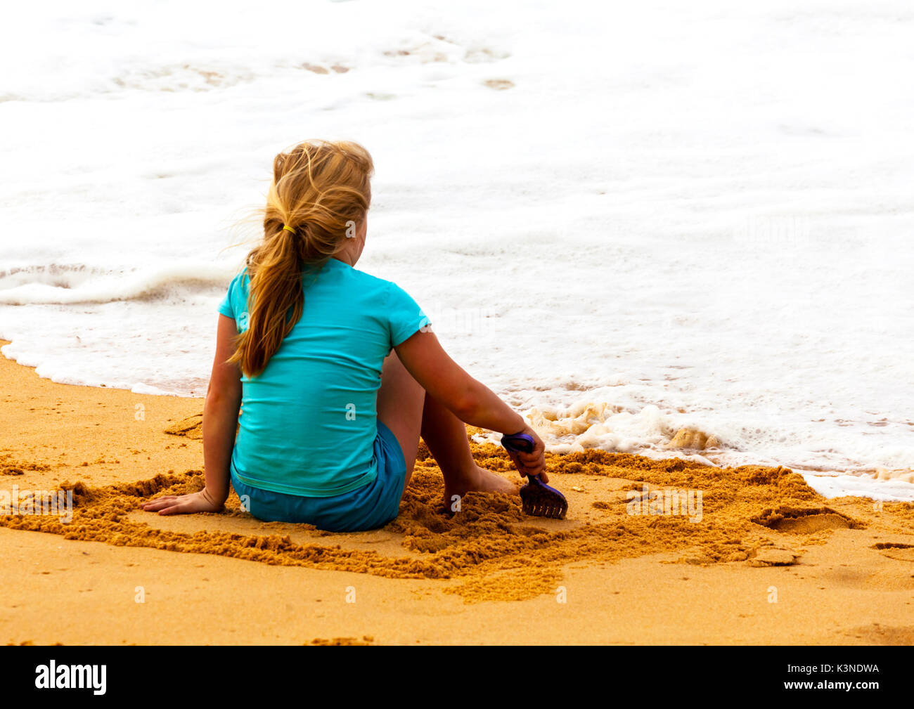 Junges Mädchen sitzt am Strand beim Warten auf die ruhigen Bedingungen zu schwimmen. Stockfoto