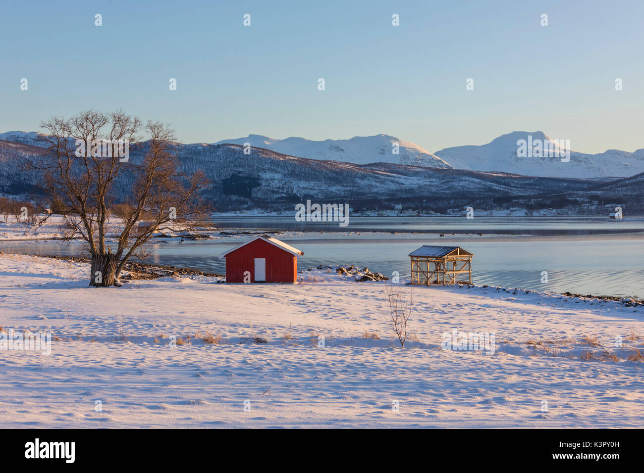 Holzhütte in der schneebedeckten Landschaft mit Blick auf die kalte See an der Straße von Gibostad an Finnsnes Senja Tromsø Norwegen Europa führende Stockfoto