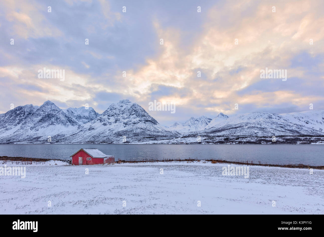 Typische Rorbu in der schneebedeckten Landschaft durch das gefrorene Meer und hohen Gipfeln Svensby Lyngen Alpen Tromsø Norwegen Europa umgeben Stockfoto