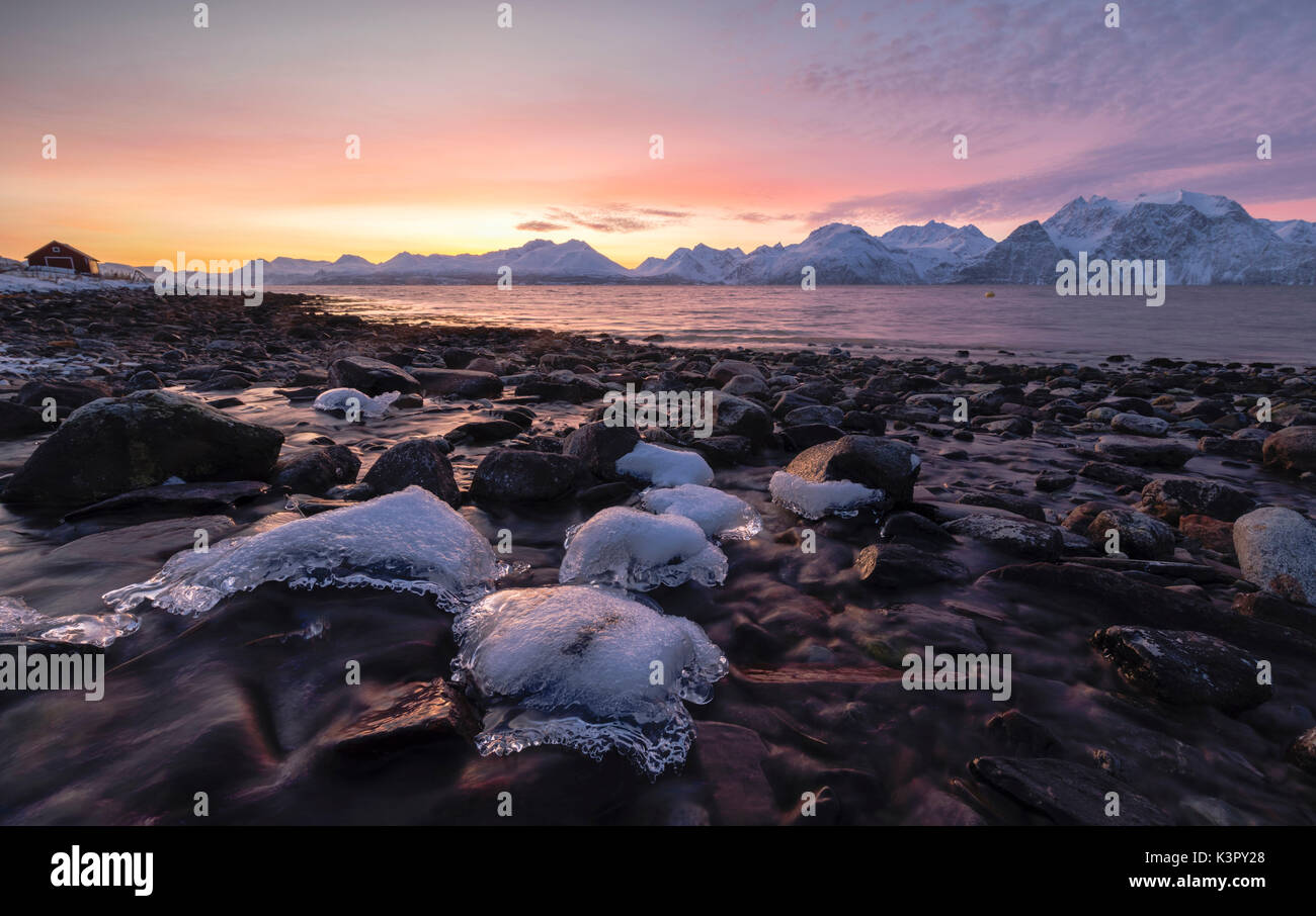 Feurige Himmel bei Sonnenuntergang auf verschneiten Gipfeln und gefrorene Meer von Felsen mit Eis Djupvik Lyngen Alpen Tromsø Norwegen Europa gerahmt Stockfoto