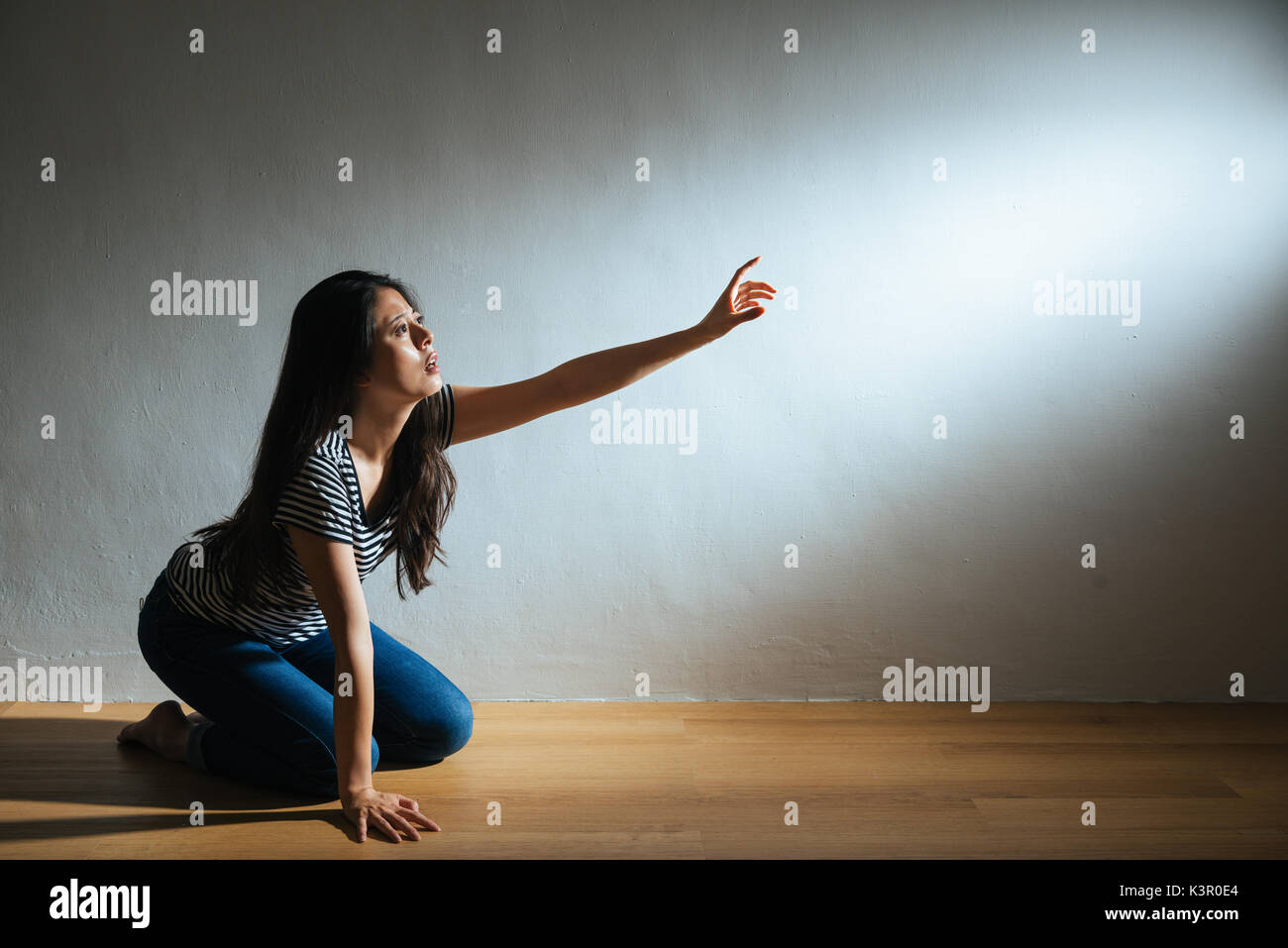 Depression lady kniend auf Holzboden Boden und Hand in den leeren Bereich auf der suche Hilfe auf der weißen Wand Hintergrund mit zerschlagenen missbraucht Licht Stockfoto