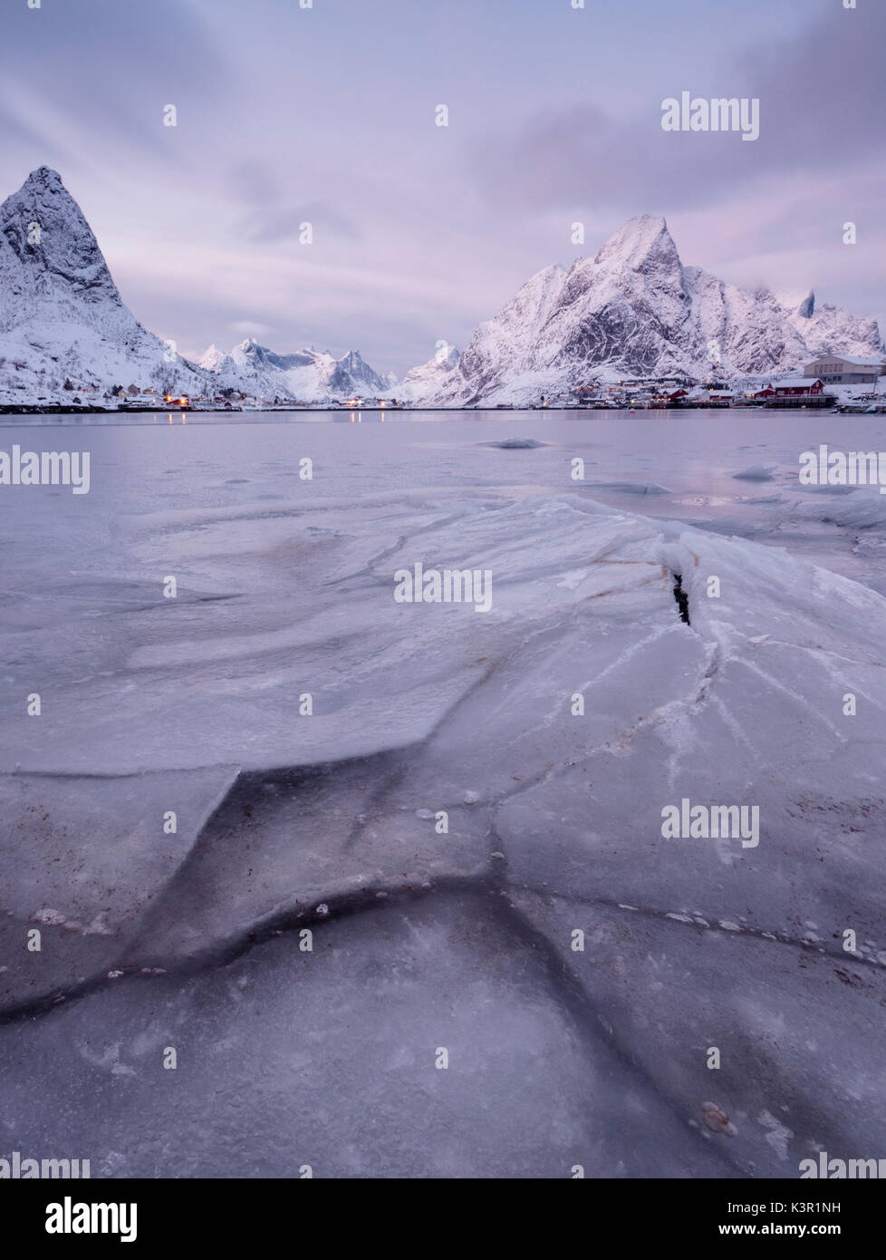 Das gefrorene Meer und die schneebedeckten Gipfel umrahmen das Fischerdorf am Sonnenuntergang Reine Nordland Lofoten Inseln Norwegen Europa Stockfoto
