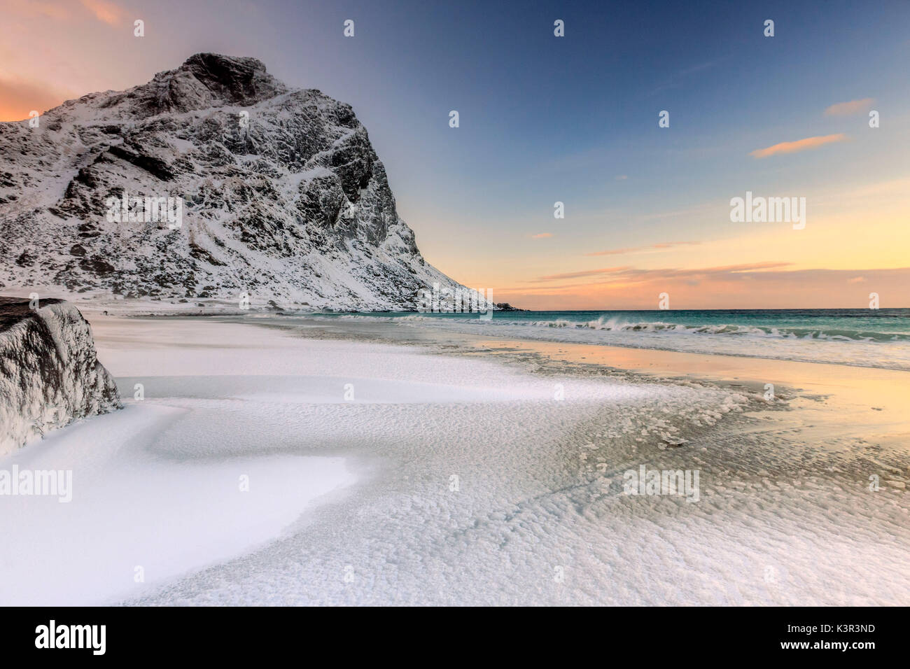 Wellen Fortschritte in Richtung Strand von schneebedeckten Gipfeln im Morgengrauen umgeben. Uttakleiv Lofoten norwegen Europa Stockfoto