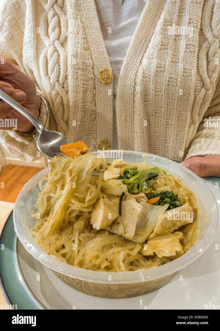 Eine Frau mit einer Gabel und einen Teller mit warmen chinesischen Gemüse Nudeln in einem Kunststoffbehälter, als Teil einer Mahlzeit zum Mitnehmen zu Hause. England, UK. Stockfoto