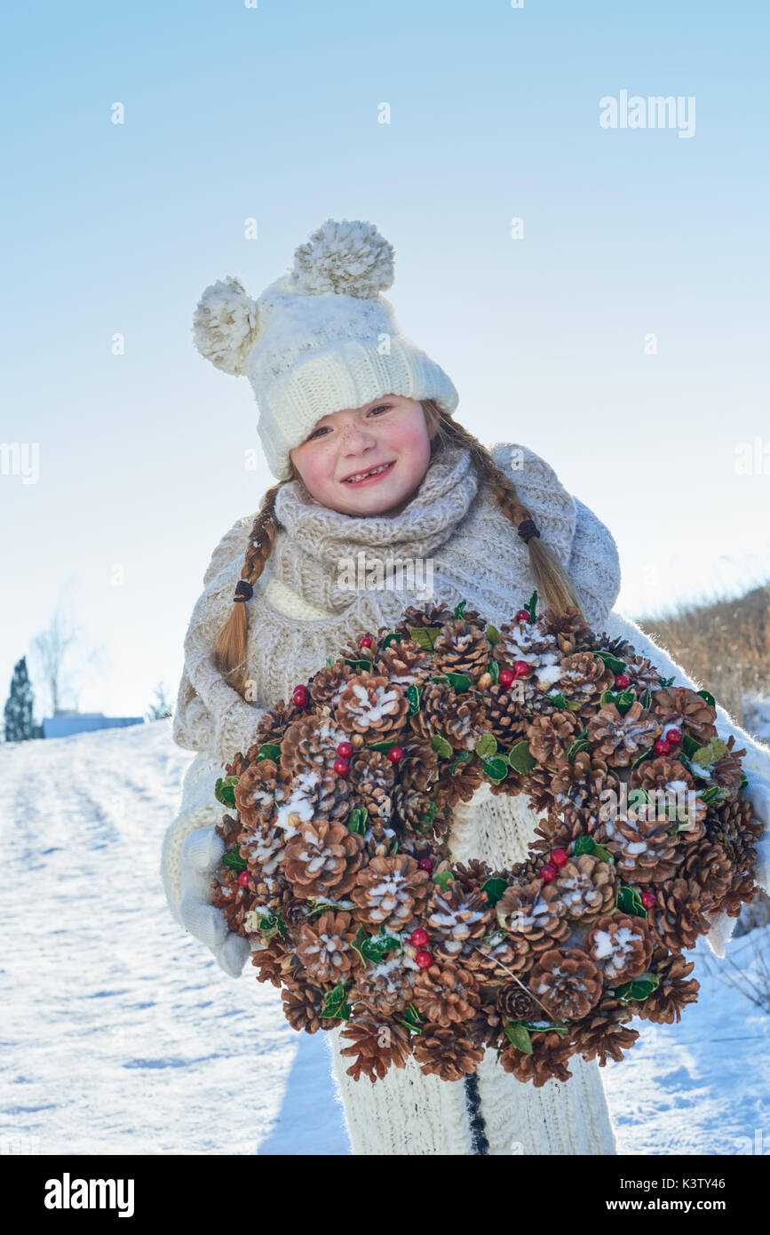 Kind stehend auf den Schnee halten Adventskranz für Weihnachten Stockfoto