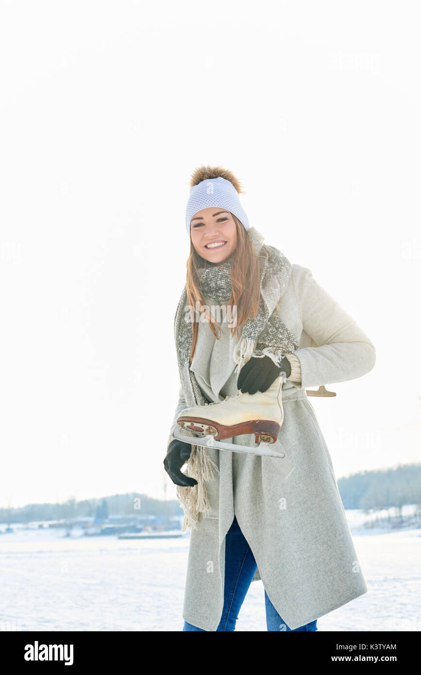 Junge Frau mit Schlittschuhen auf ihrer Schulter lächelt glücklich auf Ihrem Winterurlaub Stockfoto