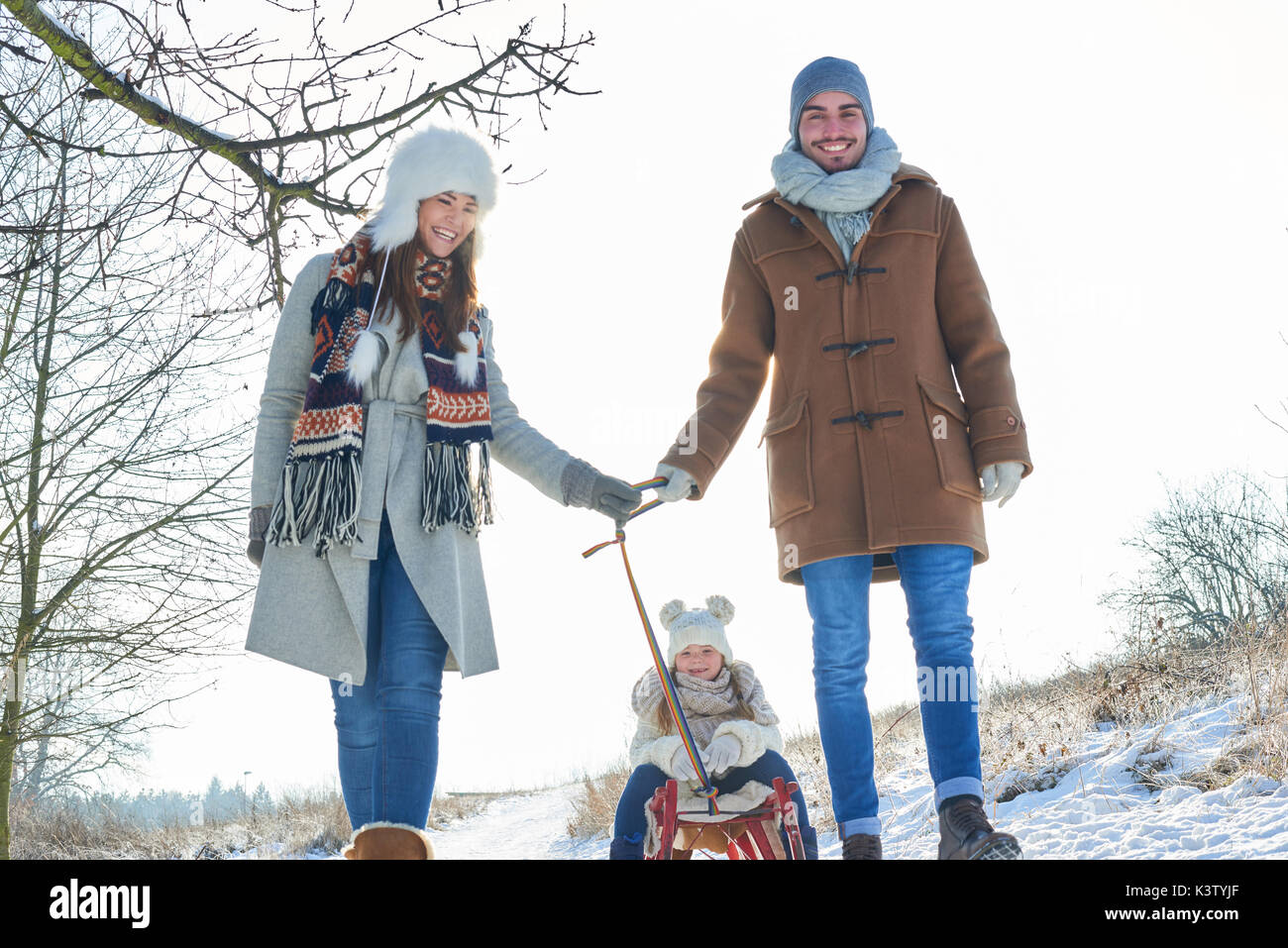 Glückliche Eltern ziehen Kind auf Schlitten auf dem Schnee Stockfoto