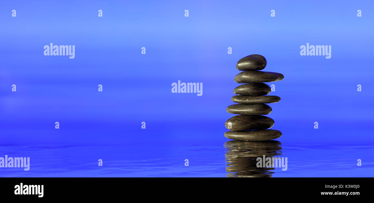 Zen Steine auf blauem Hintergrund gestapelt, Reflexionen auf dem Wasser Stockfoto