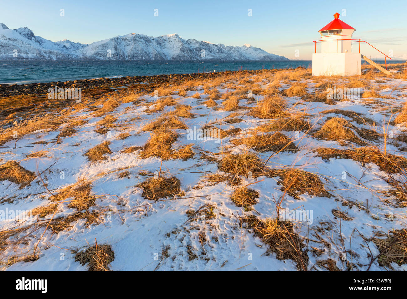 Die Sonne beleuchtet die Küste in der Nähe von einem traditionellen Leuchtturm. Spaknesora Naturreservat, Djupvik, Lyngenfjord, Lyngen Alpen, Troms, Norwegen, Lappland, Europa. Stockfoto