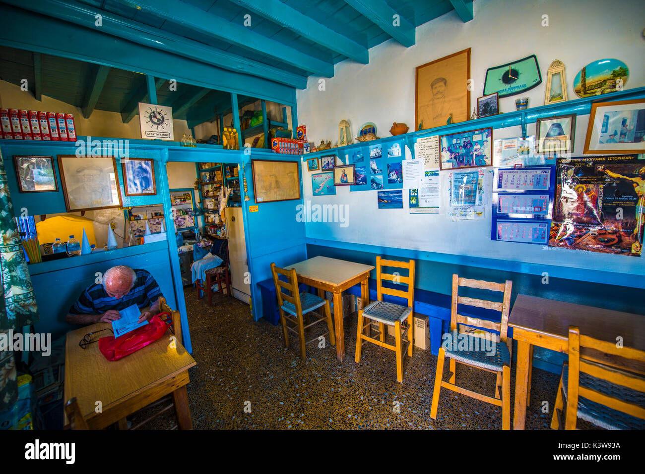 Insel Amorgos, Kykladen, Griechenland, Europa. Die Inneneinrichtung und alte Taverne mit Stühlen, Tisch und einen alten Mann lesen Stockfoto