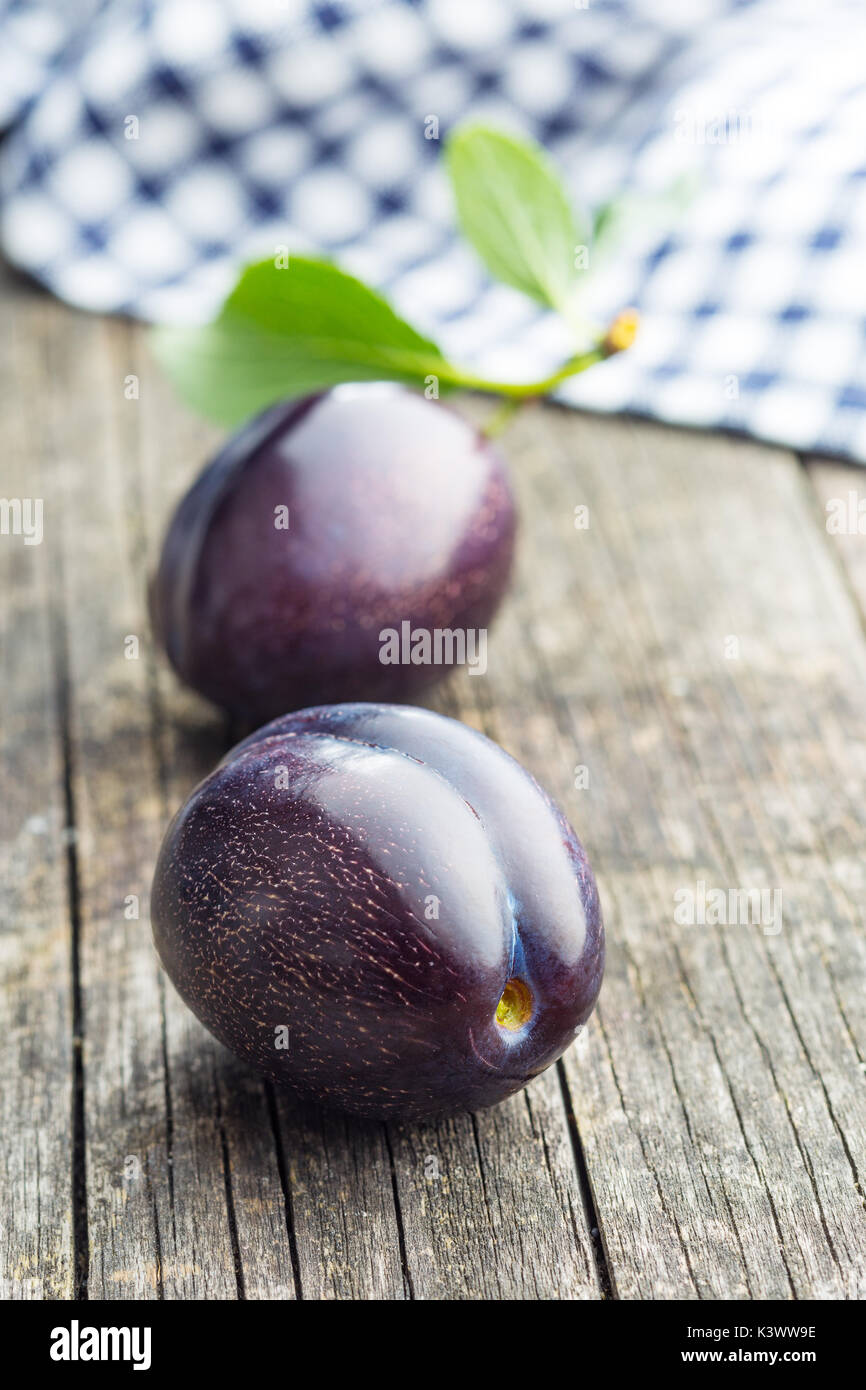 Zwei frische Pflaumen auf alten Holztisch. Blaue Pflaumen mit Blättern. Stockfoto