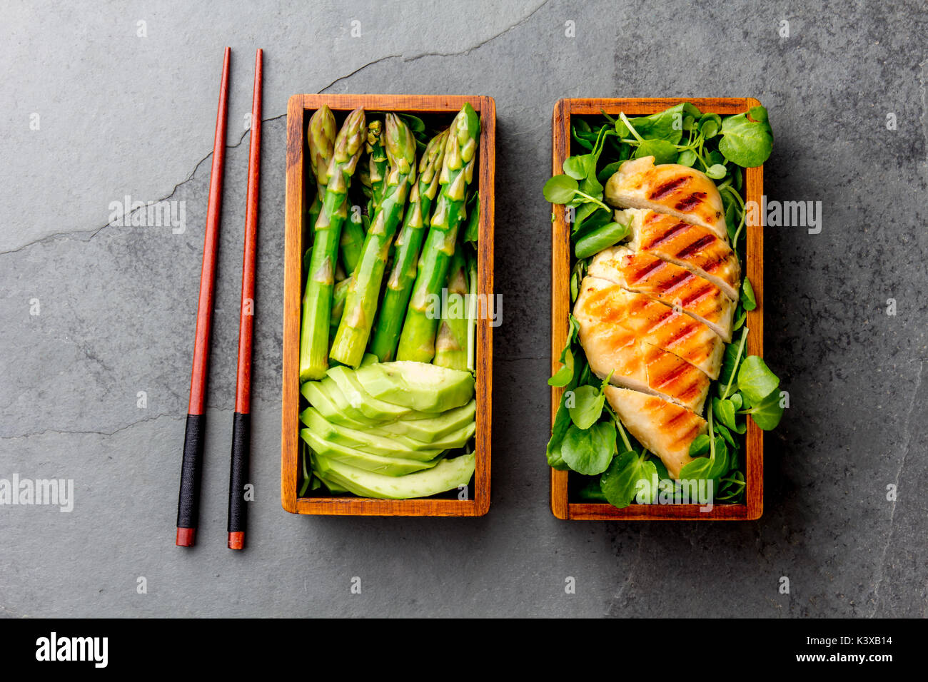 Gesundes Mittagessen in Holz- japanische Bento Box. Ausgewogene gegrillt chucken und Avocado mit Spargel und grüner Salat. Ansicht von oben, schiefergrau Bac Stockfoto