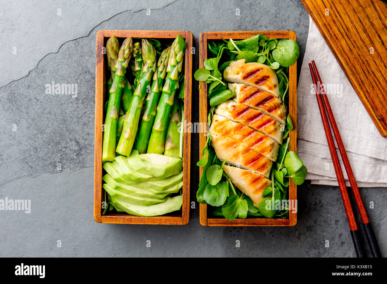 Gesundes Mittagessen in Holz- japanische Bento Box. Ausgewogene gegrillt chucken und Avocado mit Spargel und grüner Salat. Ansicht von oben, schiefergrau Bac Stockfoto