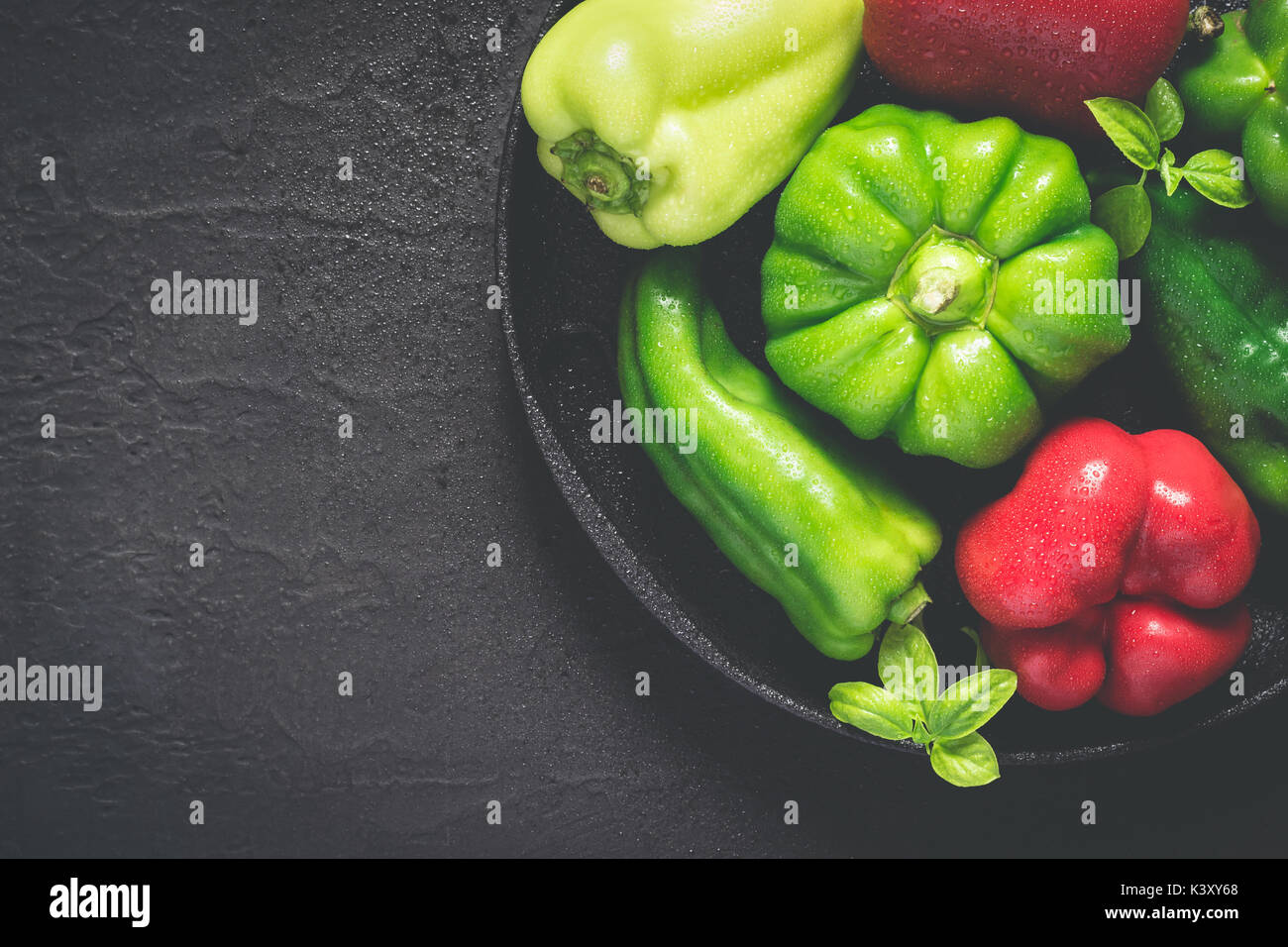 Gusseiserne Schale mit verschiedenen rote und grüne Paprika mit Wassertropfen. Stockfoto
