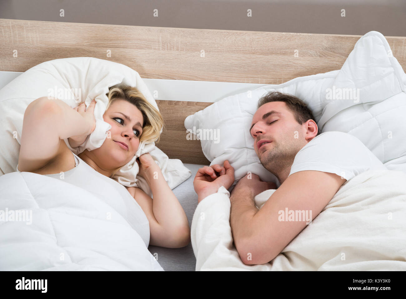 Frau, die Ohren während Mann Schnarchen in Bett zu Hause Stockfoto