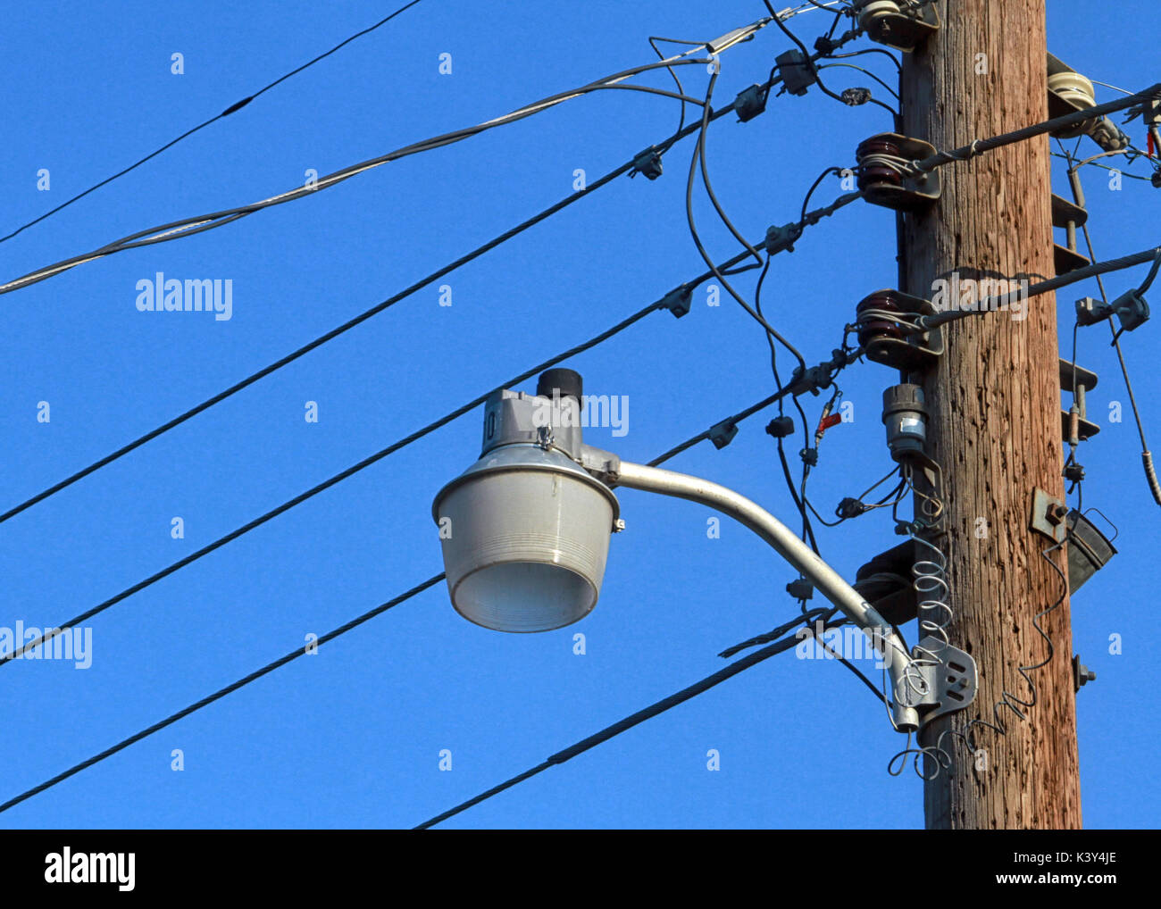 Einem unbeleuchteten Straßenlaterne auf einer hölzernen Pfosten mit Telefon Kabel zeichnet sich vor blauem Himmel. Stockfoto