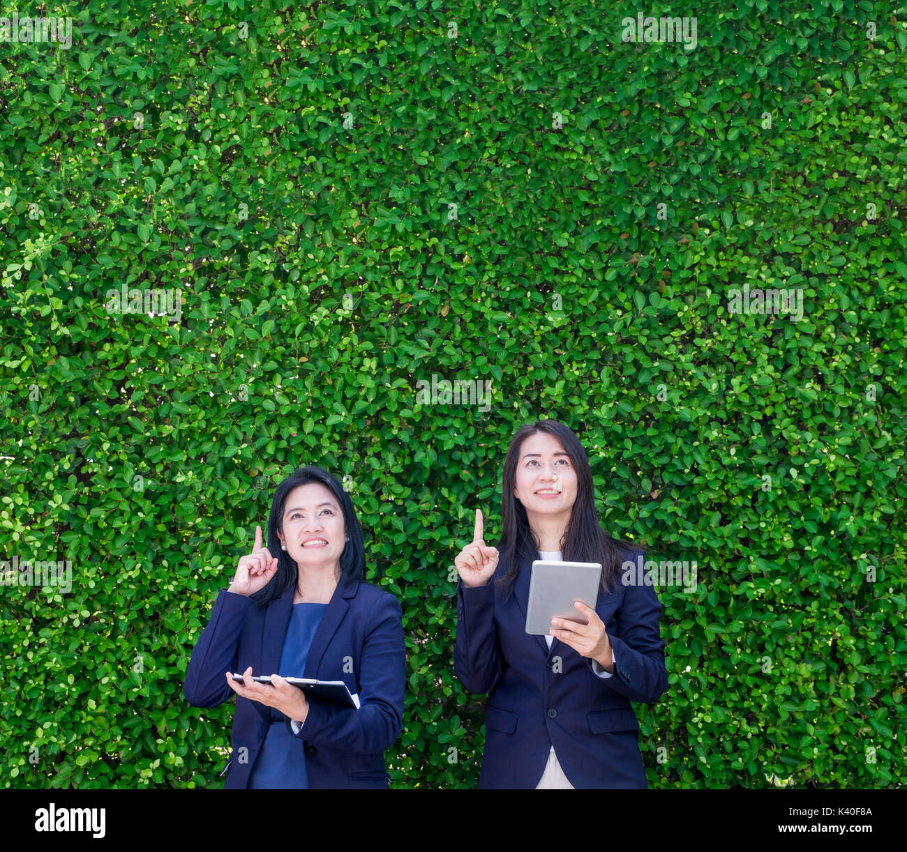Zwei asiatische Geschäftsfrau Holding Tablet und Punkt-finger bis zu Luft mit denken Action am grünen Blatt Wand, lassen textfreiraum zum Hinzufügen von Text oder Design, N Stockfoto
