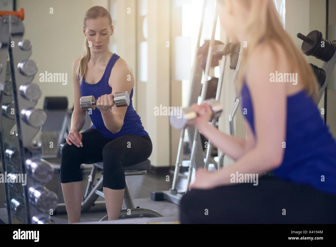 Gesunde Frau trainieren mit Gewichten vor einen großen Wandspiegel in einem Fitnessstudio drehen, um über die Schulter in die Kamera schauen, wie sie zwei d hält fit Stockfoto