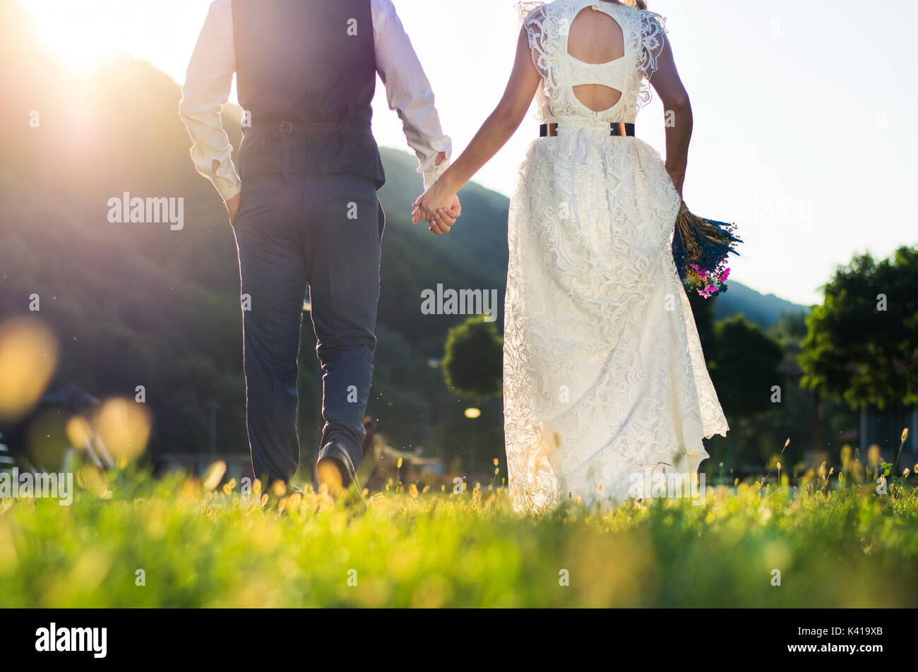Braut und Bräutigam in Richtung Sonnenuntergang halten sich an den Händen Stockfoto