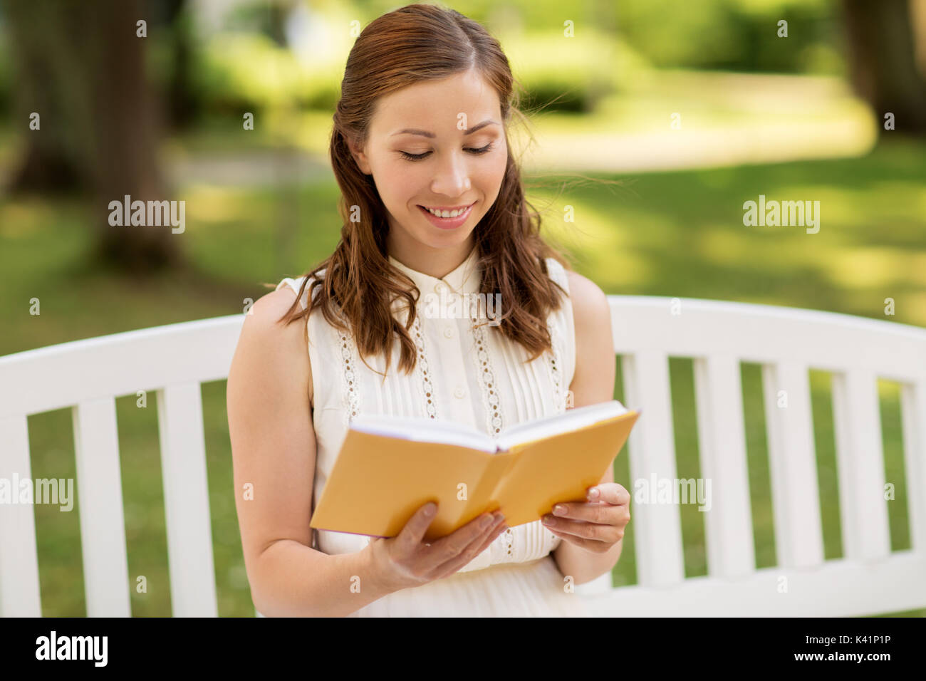 Lächelnde junge Frau liest Buch im Sommer Park Stockfoto