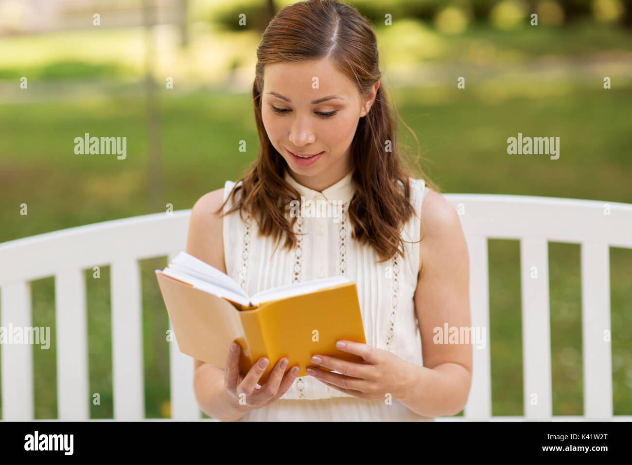 Lächelnde junge Frau liest Buch im Sommer Park Stockfoto