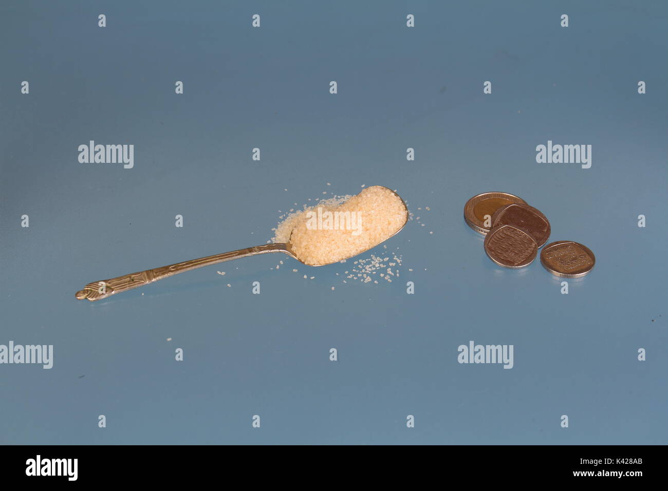 Einen gehäuften Teelöffel mit goldenen Zucker Neben einigen Silbermünzen auf einen klaren Hintergrund mit Kopie Raum im Querformat. Stockfoto