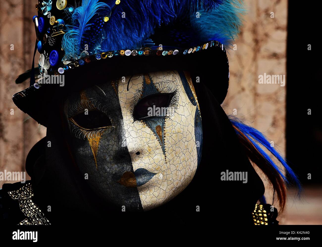 Eine Person im Kostüm an der Karneval von Venedig, trug einen schwarzen Hut mit Knöpfen, Sicherheitsnadeln und blaue Federn geschmückt. Stockfoto