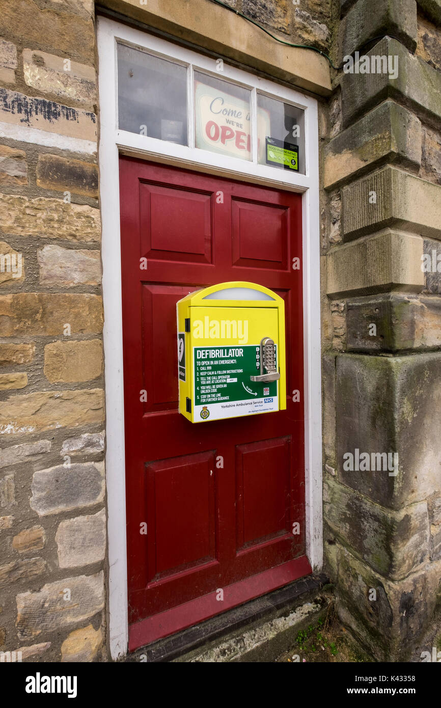 Öffentlichen Defibrillators in einem gelben Feld zu einer Tür im Stadtzentrum von Richmond, North Yorkshire Dales, England, Großbritannien Stockfoto