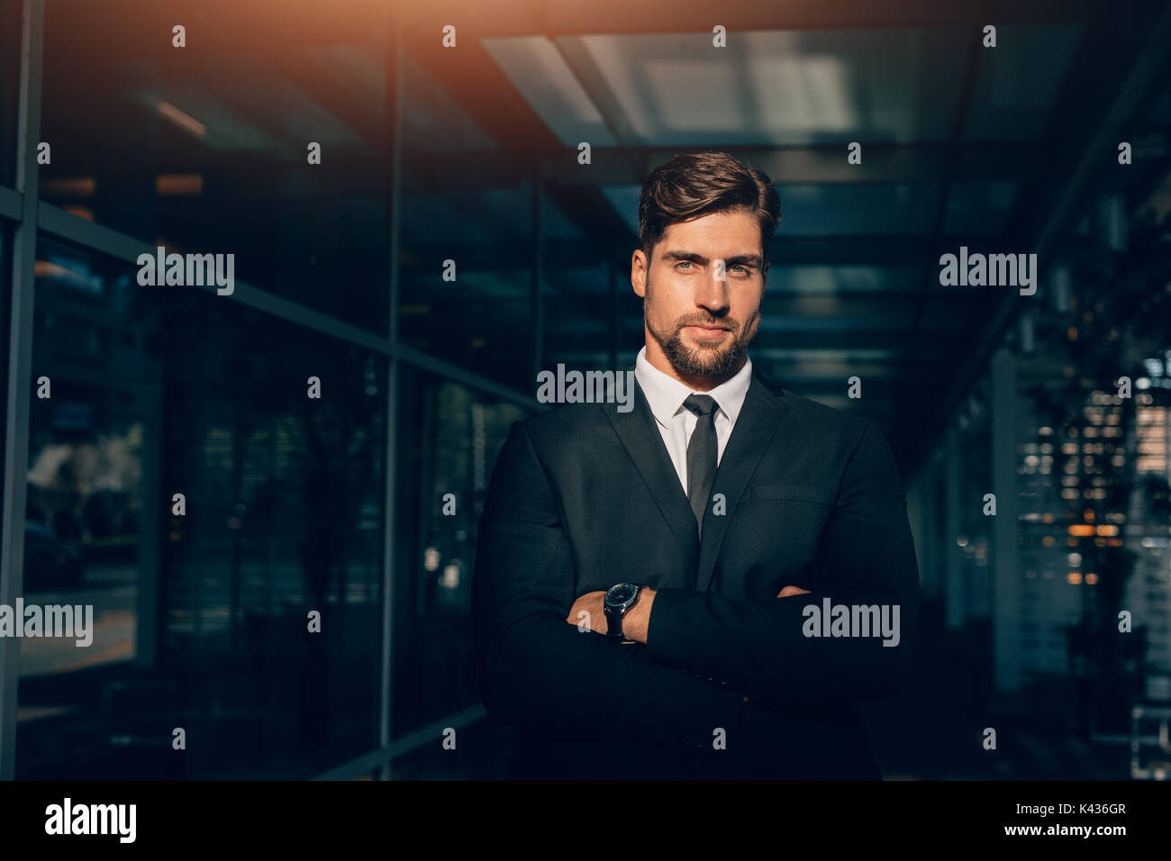 Portrait von stattlicher Junge Unternehmer Stehen mit verschränkten Armen und Kamera. Kaukasische männliche Führungskräfte stehen in einem modernen Gebäude. Stockfoto